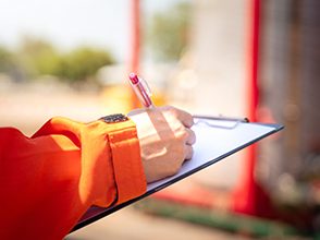 Action of safety officer or supervisor is taking note during safety audit in oil field operation, Close-up and selective focus at people's hand. Photo is appiled with orange shade sun light effect.