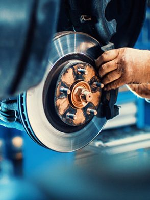 Closeup of unrecognizable mechanic replacing car brake pads. The car is lifted with hydraulic jack at eye level.