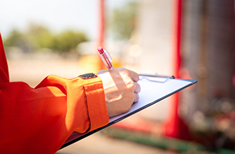 Action of safety officer or supervisor is taking note during safety audit in oil field operation, Close-up and selective focus at people's hand. Photo is appiled with orange shade sun light effect.