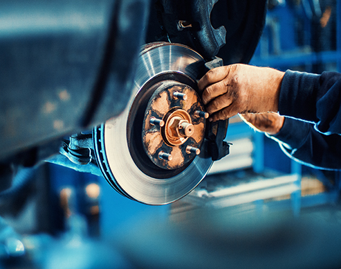 Closeup of unrecognizable mechanic replacing car brake pads. The car is lifted with hydraulic jack at eye level.